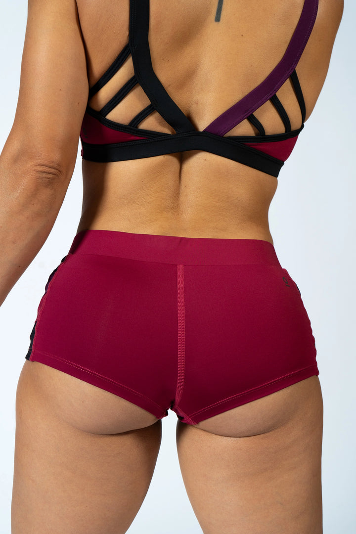 Woman wearing magenta sports bra and shorts with black accents on a plain background #color_red-wine