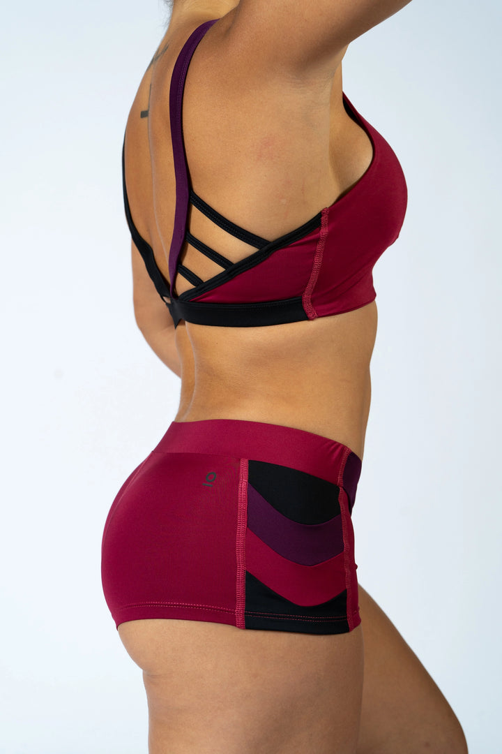 Woman wearing magenta sports bra and shorts with black accents on a plain background #color_red-wine