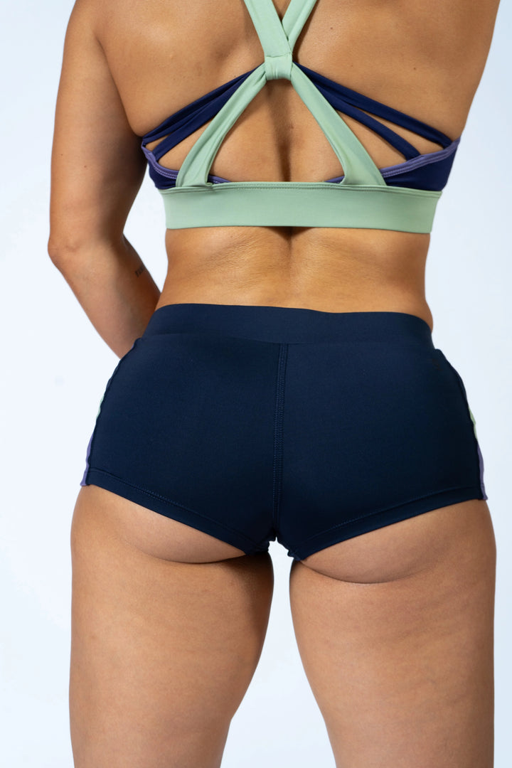Woman wearing blue sports bra and blueshorts  on a plain background #color_iris-mystical-basil