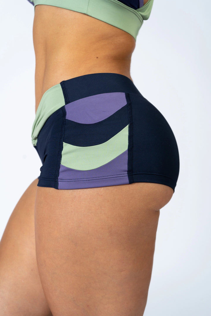 Woman wearing blue sports bra and blueshorts  on a plain background #color_iris-mystical-basil