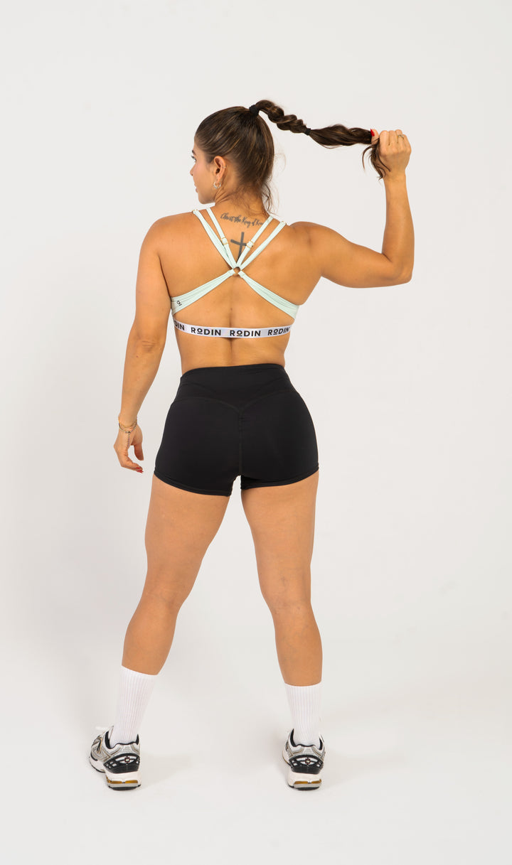 Woman wearing a sports bra and shorts with visible branding on a white background. #color_mint