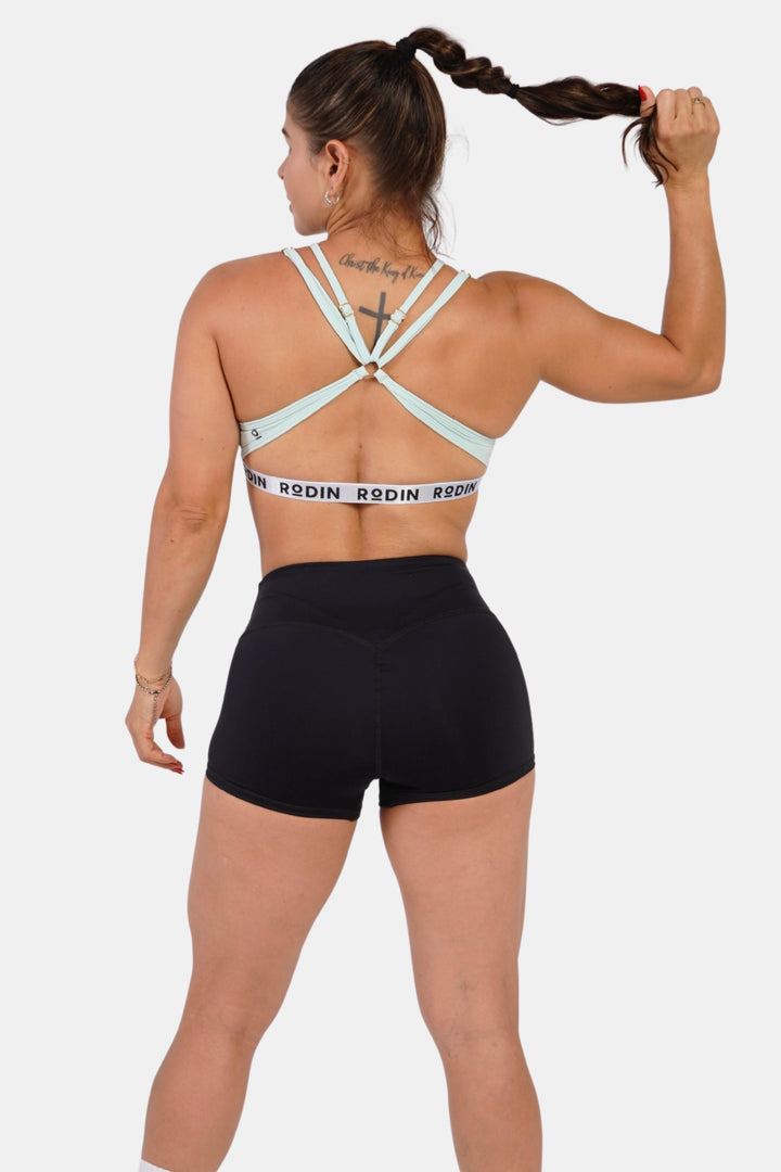 Woman wearing a light green sports bra and black shorts on a white background #color_mint