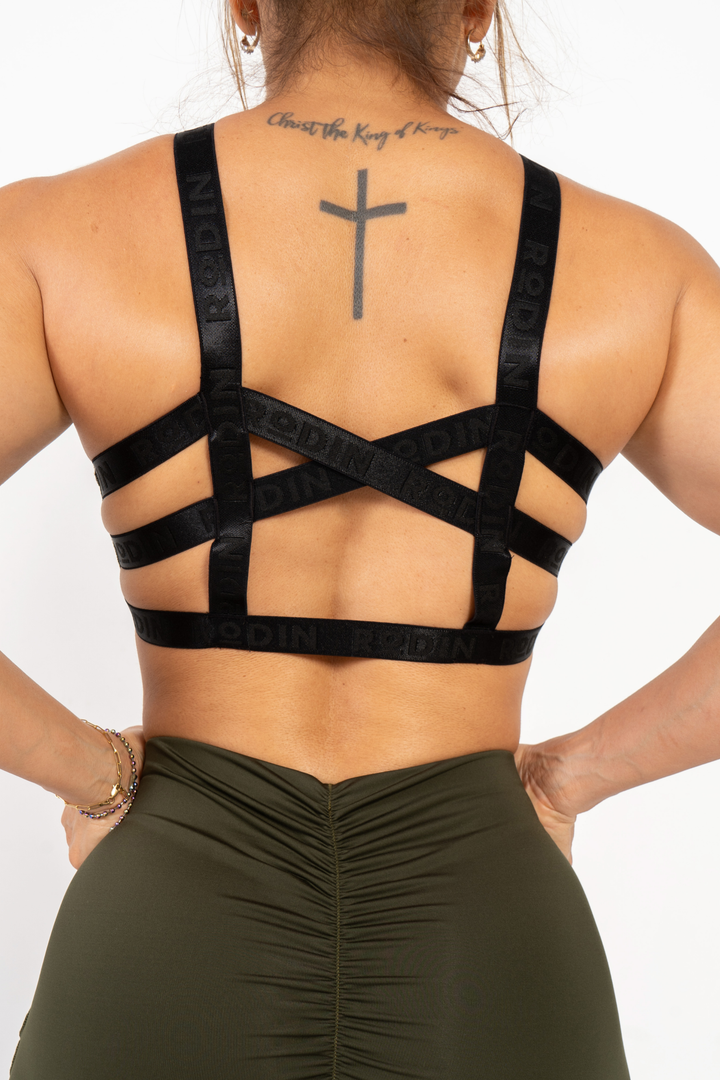 Person wearing a black strappy top and green pants on a white background 