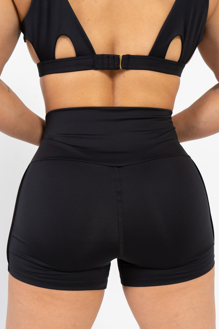 Person wearing a black sports bra and shorts set on a light gray background 
