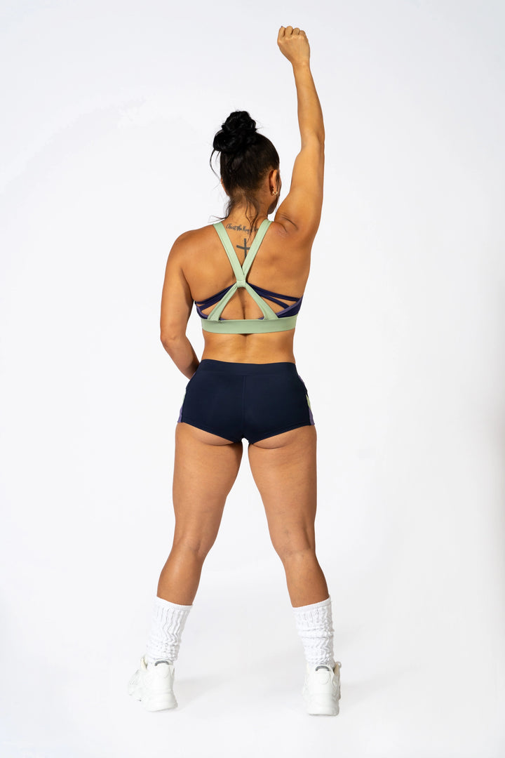 Woman wearing blue sports bra and blueshorts  on a plain background #color_iris-mystical-basil