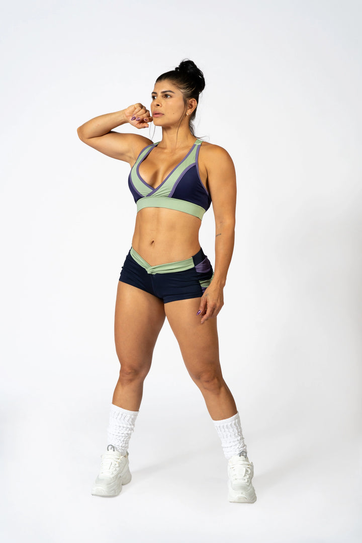 Woman wearing blue sports bra and blueshorts  on a plain background #color_iris-mystical-basil